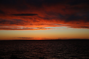 Colorful landscape at sunset.Ornate, lush, voluminous clouds cleared the horizon to the sun falling in a glittering ripple of water.The struggle of colors over the lake at the end of the day.Russia