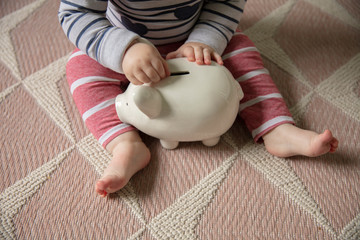 A baby puts money into a piggy bank saving for their future