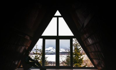 Fototapeta premium traveler relaxing near window in cozy wooden cottage with snowy mountains view.