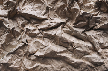 Background from very strongly crumpled light brown rough vintage paper. Textured surface made from recyclable materials resembling a mountainous terrain.
