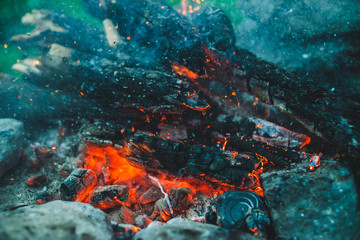 Vivid smoldered firewoods burned in fire close-up. Atmospheric background with orange flame of campfire. Full frame image of bonfire. Warm whirlwind of glowing embers and ashes in air. Sparks in bokeh