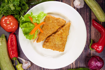 Tasty pieces of yellow cheese coated in breadcrumbs and fried in a plate on a wooden table, top view