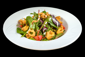 tasty squid salad with tomatoes, arugula and sauce on a white plate, isolated on a black background.