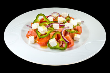 tasty summer salad with tomatoes, fresh pepper, cheese, onion and olive oil on a white plate, isolated on a black background.