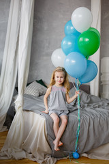 Fototapeta na wymiar A little girl standing with balloons in the bedroom. A child is playing in his bedroom with colorful balloons. Concept of childhood, birthday at home, home holiday.