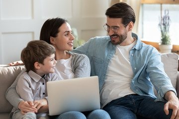 Happy young family with little preschooler son sit relax on couch in living room have fun using...