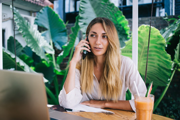 Pensive woman speaking on smartphone in resort cafe