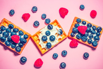 Sweet Homemade waffles with fresh raspberries, blueberries and cream on pink background