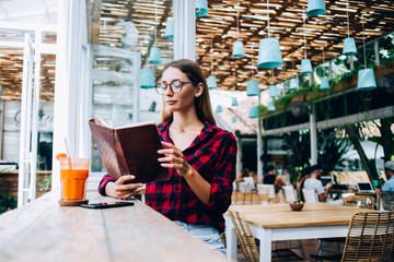 Smart woman in round glasses reading book in cafe