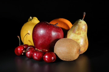 Fruit still life with a black background consisting of: orange, apple, lemon, pear, kiwi and cherries