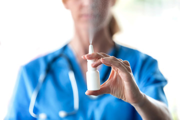 Female doctor with a spray or nasal drops for the treatment of a runny nose over white background. - obrazy, fototapety, plakaty
