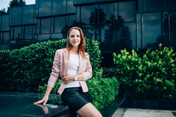 Portrait of elegant female manager 20s posing on urban setting architecture recreating outdoors, formally dressed redhead caucasian beautiful woman student looking at camera during leisure