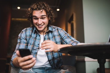 Smiling amazed hipster guy influencer amazed with followers message holding mobile phone, positive...