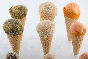 organic handmade ice cream cones in four flavors and different sizes on a stand. The flavors are chocolate, pistachio, caramel and mango. Close up - 349817424