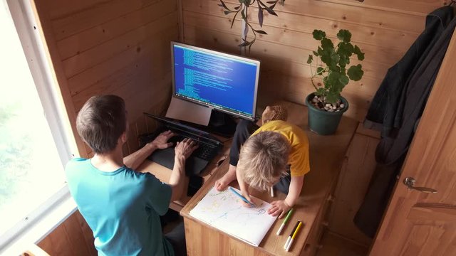 father developer work from home on computer, small child sits near and paint, concept of stay home in quarantine isolation, self-isolated family candid lifestyle, parenthood difficulties