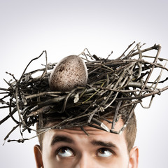 Male holds a birds nest on his head. On grey background.