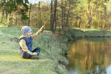 Naklejka na ściany i meble a boy on the riverbank in the forest plays with an improvised fishing rod, concept happy family camping in the forest