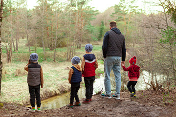 young man and children look at the river from a cliff in the forest, dad and four children, paternity leave