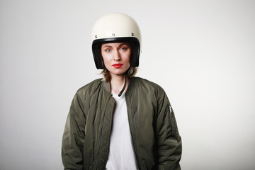 Caucasian biker young woman, wearing retro helmet, with red lips posing over white wall. Space for your text.
