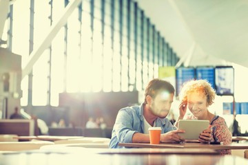 Couple using digital tablet while waiting for their flight in airport with lens flare

