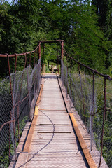 Obraz premium Old suspension bridge over the small river is leading to the forest