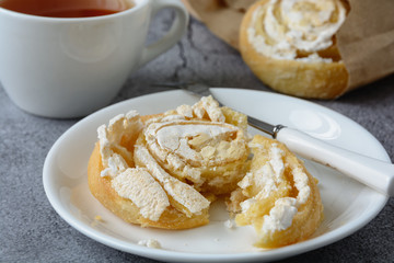 Cake in the form of a snail with curd filling topped with sugar icing is in a white ceramic plate next to a cup of tea