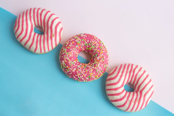 Group of colourful glazed doughnuts lies on pink and blue background. Horizontal photography. Theme of delivery from Fast Food Restaurant