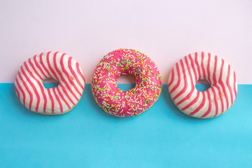 Group of colourful glazed doughnuts lies on pink and blue background. Horizontal photography. Theme of delivery from Fast Food Restaurant