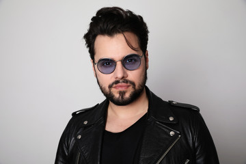 Obraz premium Bearded man in the leather outfit with bright white t-shirt wearing stylish spectacles posing over white wall. Isolated.