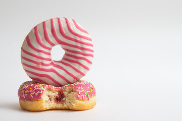 Fototapeta na wymiar Two colourful glazed doughnuts lies on white background. One of them is bitten. Horizontal photography. Copy space for your text. Junk Food Theme.