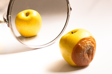 Apple in good condition looking at itself in the mirror while its back is rotten. Psychological concept, deception - obrazy, fototapety, plakaty