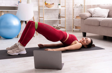 Interactive home workout. Latin girl watching live stream training and doing abs exercise with...
