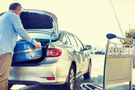 Portrait Of Mature Businessman Putting His Luggage On Car Trunk With Lens Flare
