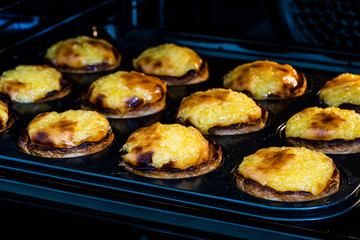 Pasteis de Nata or Belem Tart. Portuguese Custard made with Egg, Cinnamon, Sugar and Flour in Muffin Tray / Cupcake Mol in Oven.