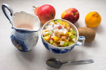 fruit salad serving in a Cup decanter milkman with fresh milk yogurt and a metal spoon isolate on a white background kiwi nectarine pear Mandarin