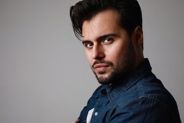 Side portrait of bearded man in the denim outfit which mixed with bright white t-shirt posing over white wall. Isolated.