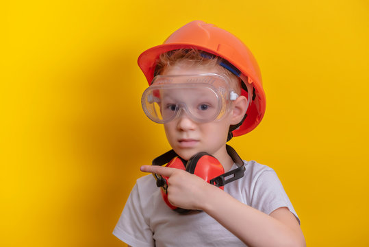 Cute Boy In Builder Glasses, Helmet And Headphone To Ear Protection Shown Finger Up Over Yellow Background  Copy Space