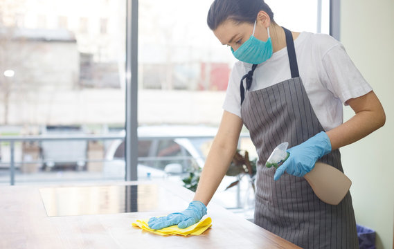 Woman in blue protective rubber gloves is spraying disinfectant