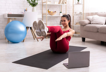 Fitness instructor streaming at-home workout online via laptop, doing abs exercise