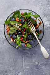 Fresh lettuce leaves with blueberries and pomegranate seeds in a bowl, top view.