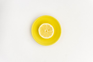 Fresh lemon in a vivid yellow dish isolated on white. Minimal summer yellow concept.