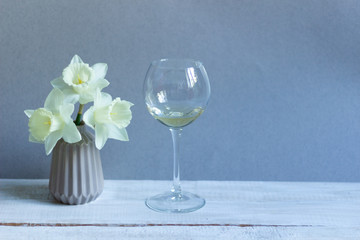 White wine in glass with vase of daffodils on beige background