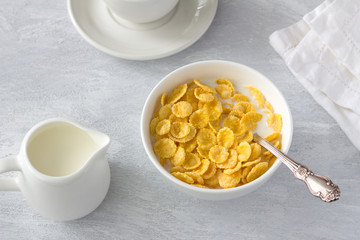 Sweet crunchy cornflakes with milk on a gray textured background. Fast tasty breakfast, top view, horizontal	