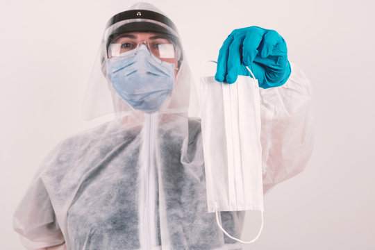 Corona virus pandemic concept: Laboratory scientist with blue mask, medical hygienic protection gloves and protective glasses holding and giving away a white face mask 