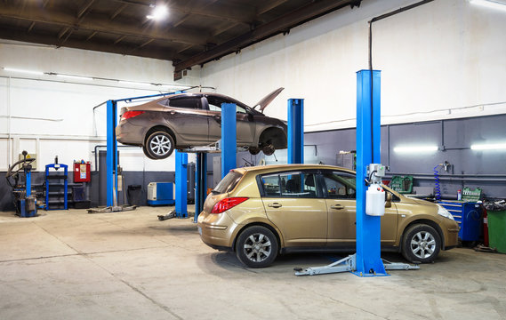 Car on lift in mechanic shop or garage, interior of auto repair workshop, vehicles inside maintenance.