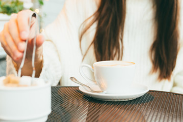 The hand of a young girl who takes refined sugar to put in a cup of coffee. Middle plan, focus on a cup of coffee.