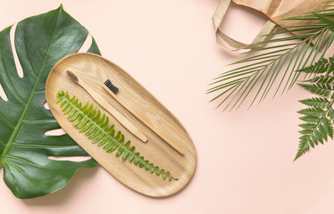 Flatlay design of morning accessories, toothbrush, hairbrush on bamboo plate with dry tropical...