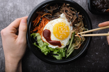  Korean dish bibimbap. Top view close up. Hands holding korean sticks.