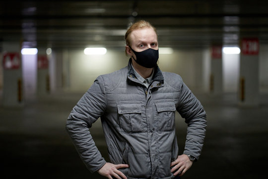 Man In A Black Mask To Protect Herself From The Covid-19 Coronavirus During Pandemic And Posing In A Grey Jacket At An Underground Parking In Russia.     