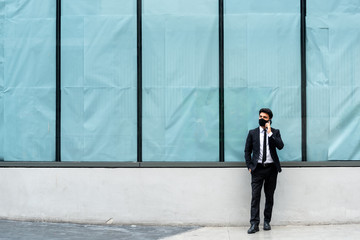 Fototapeta na wymiar Businessman wearing black mask use smartphone standing near a closed department store window during corona virus outbreak lock down